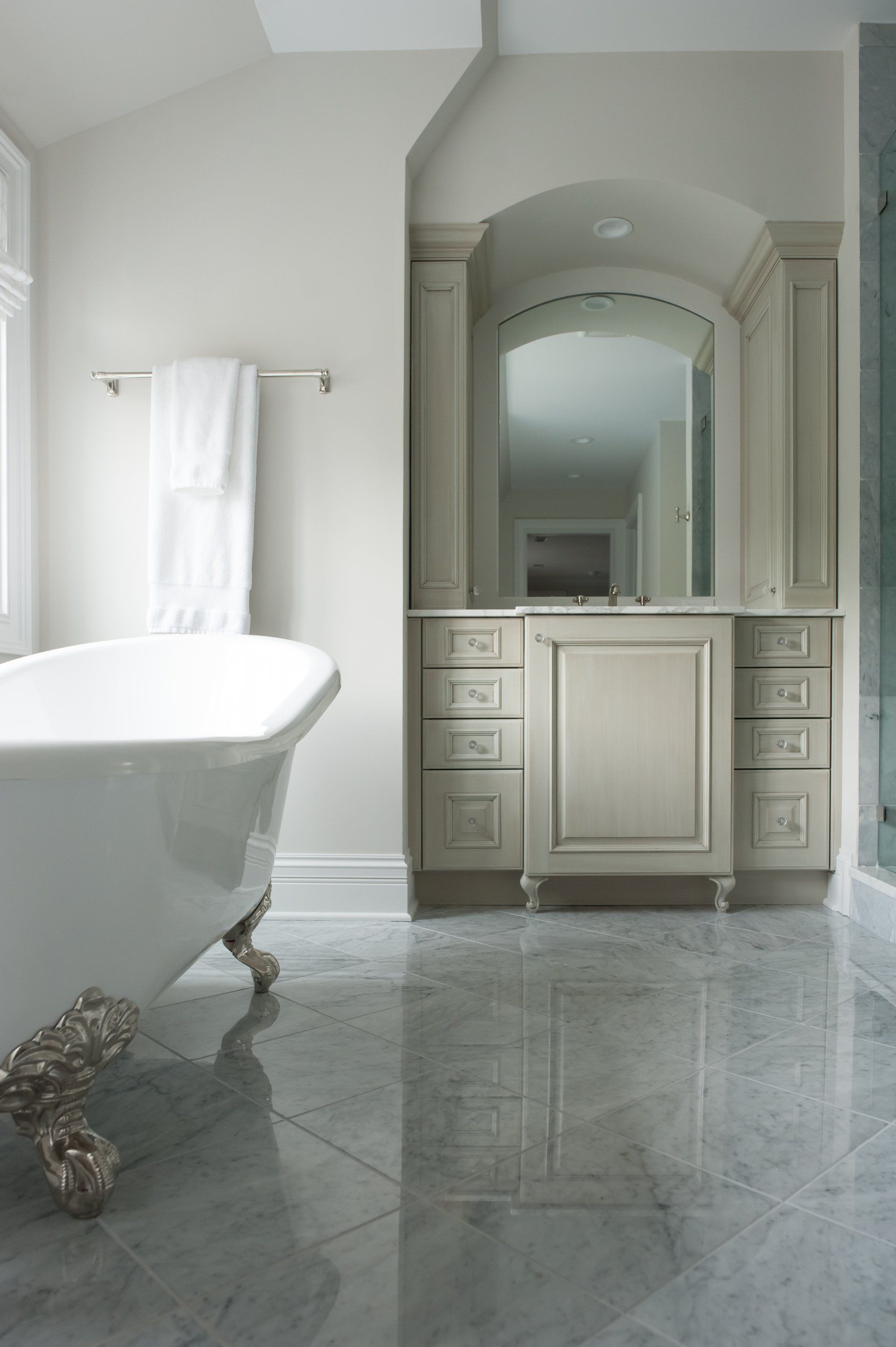 A bathroom with a bathtub , vanity , mirror and cabinets.