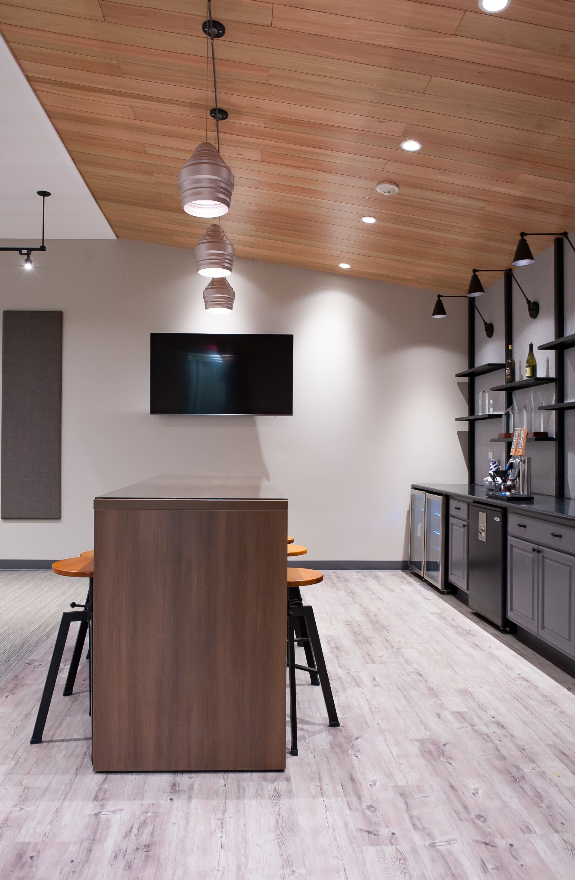 A kitchen with a table , stools , and a flat screen tv on the wall.