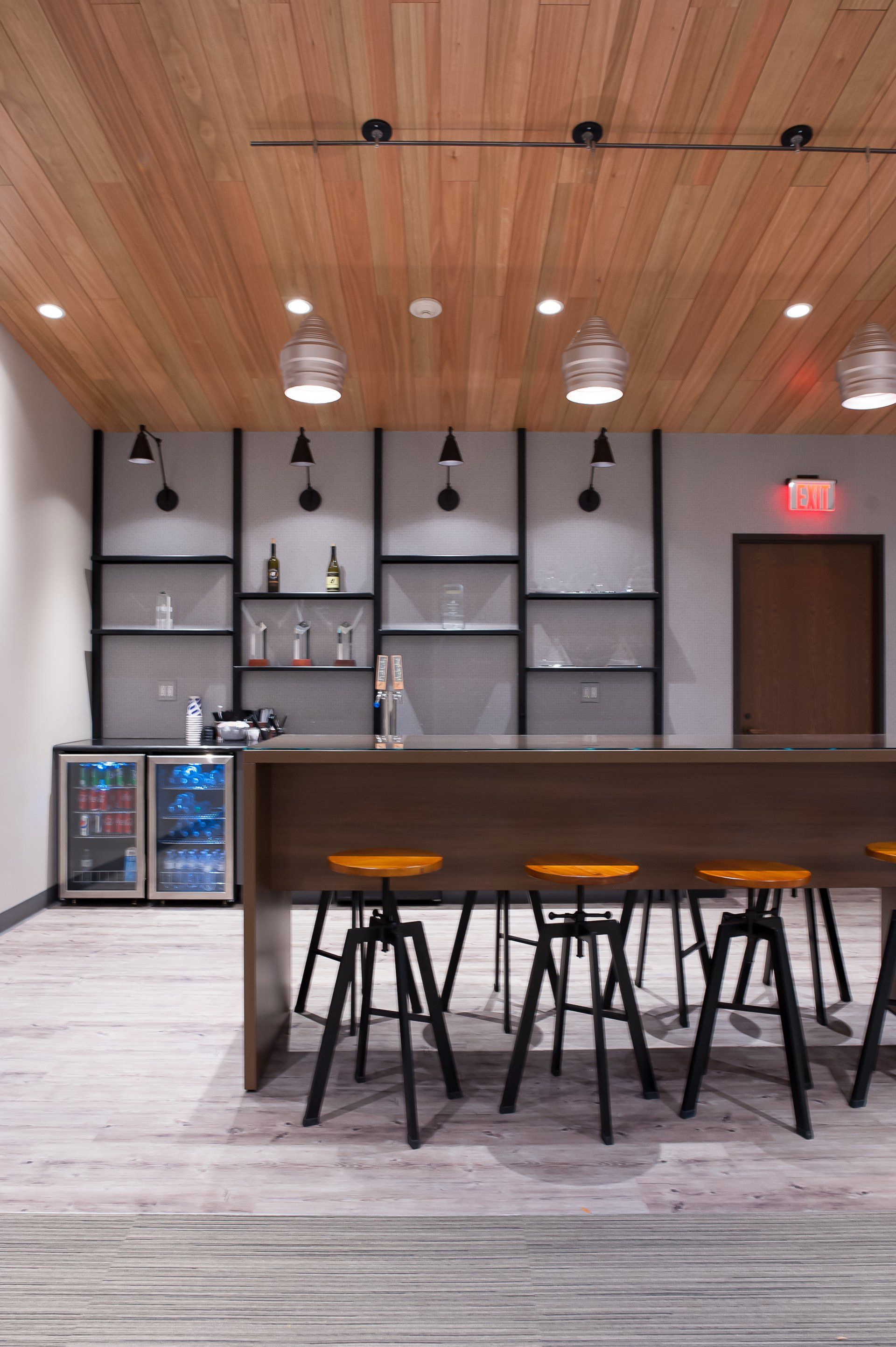A room with a long table and stools and a refrigerator.