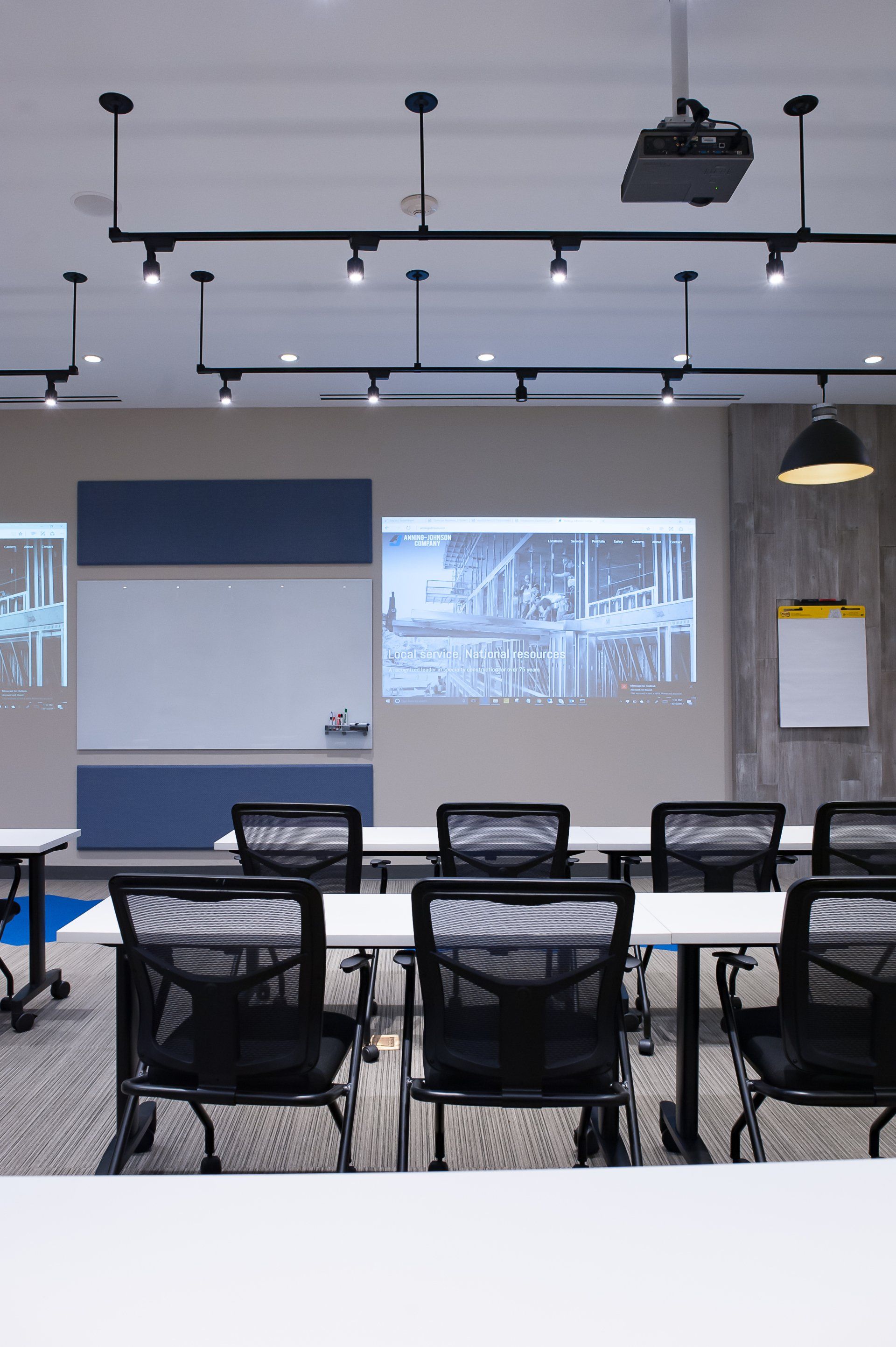 A classroom with tables and chairs and a projector screen on the wall.