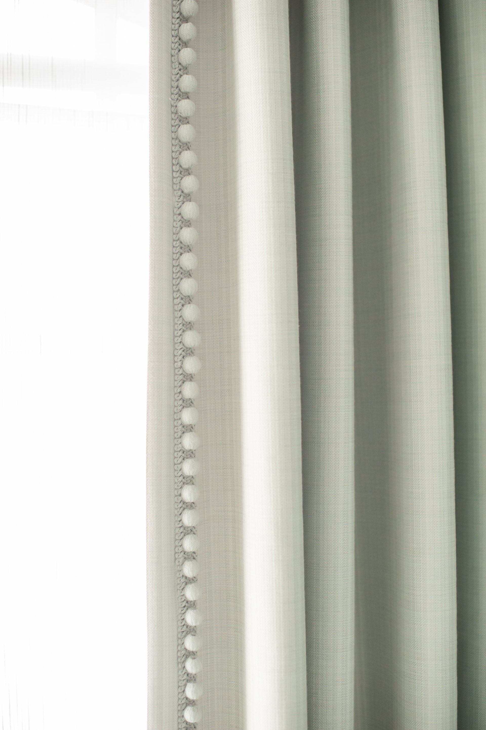 A close up of a pair of white curtains with white pom poms.