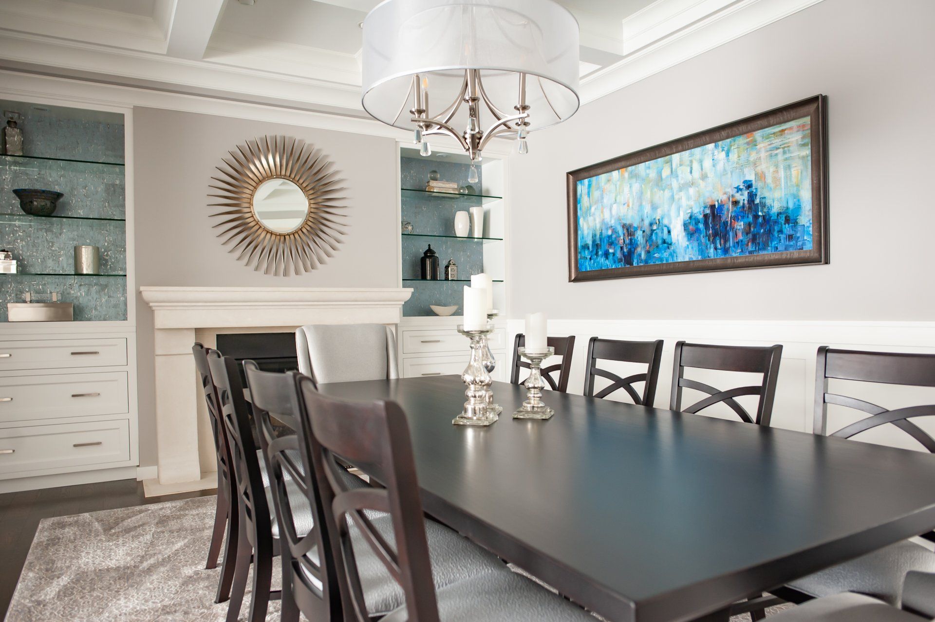 A dining room with a table and chairs and a painting on the wall.