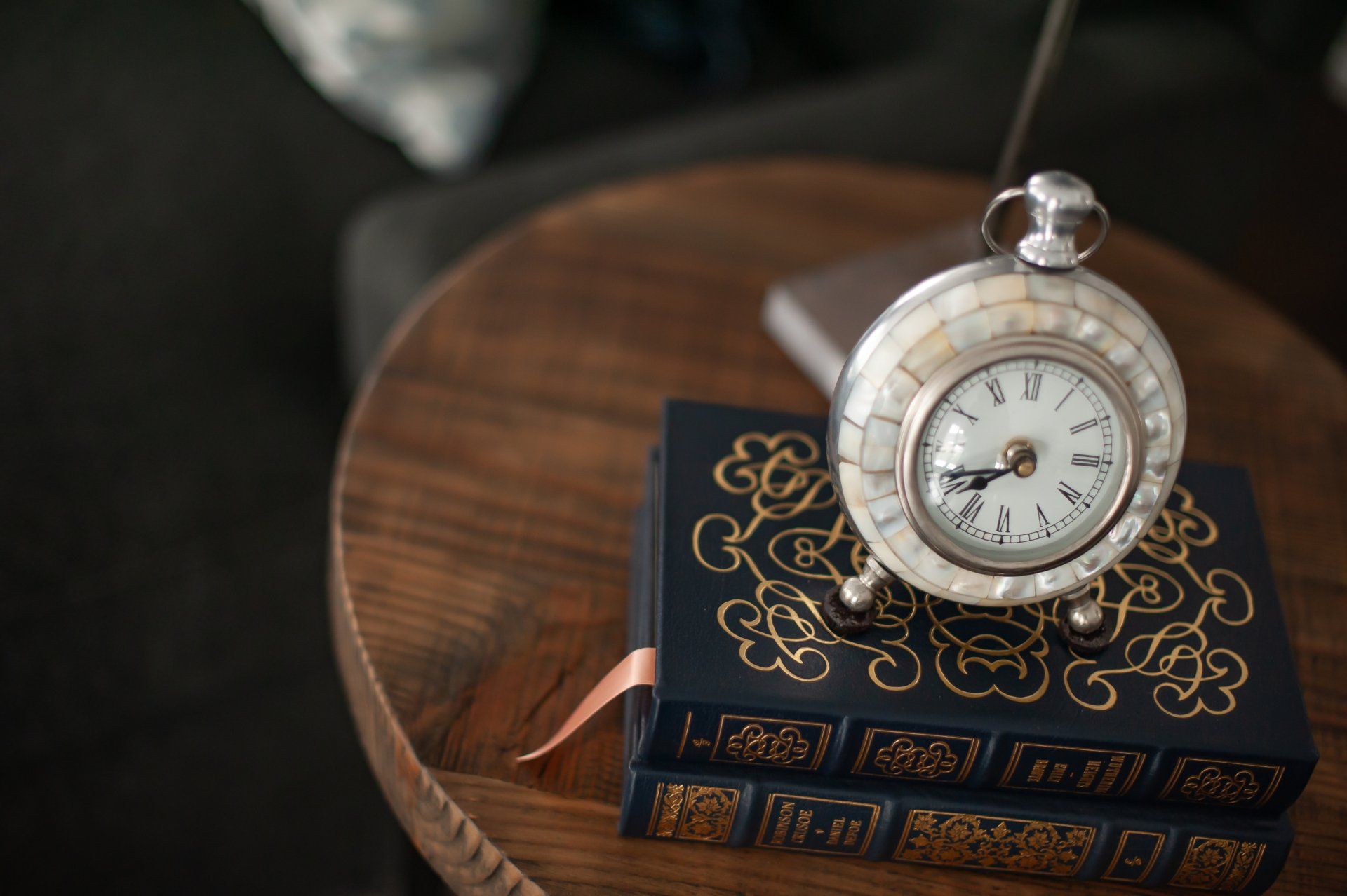 A pocket watch is sitting on top of a stack of books on a wooden table.