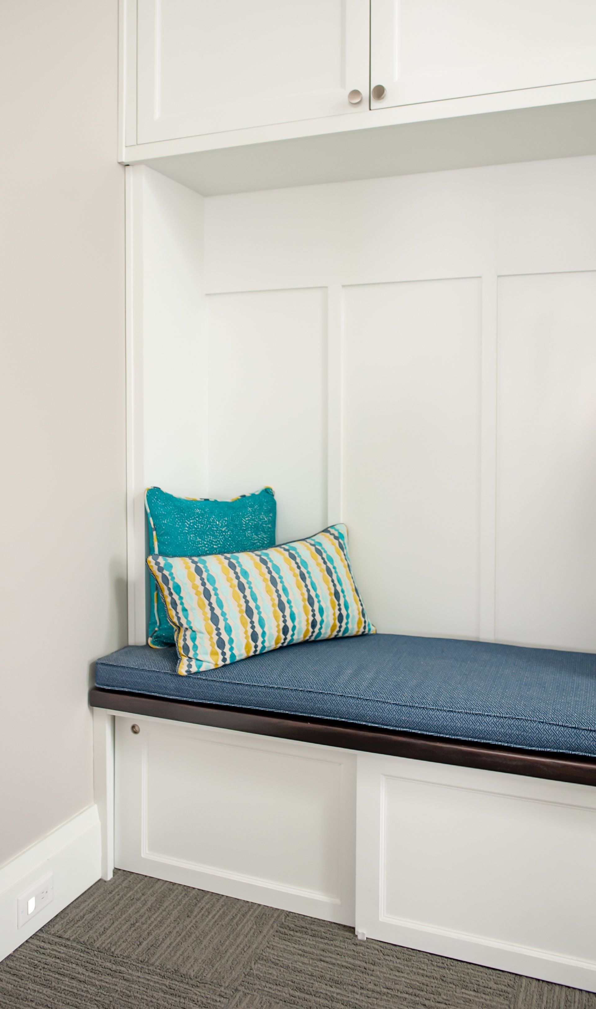 A bench with a blue cushion and two pillows in a room.