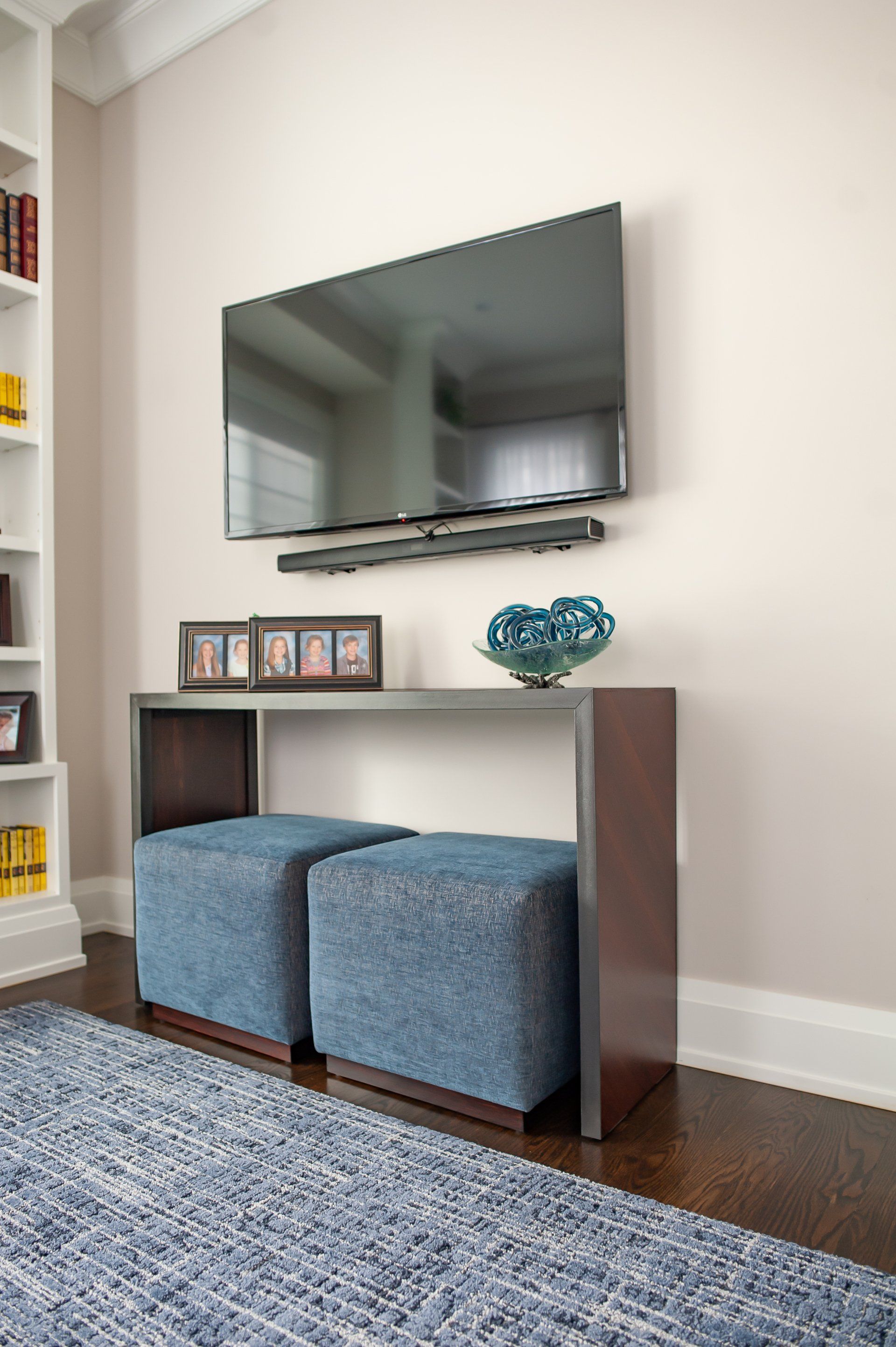 A living room with two blue ottomans and a flat screen tv on the wall.