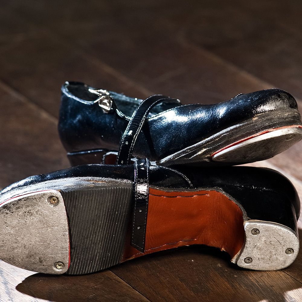 Black tap shoes with silver taps, on a wooden floor.