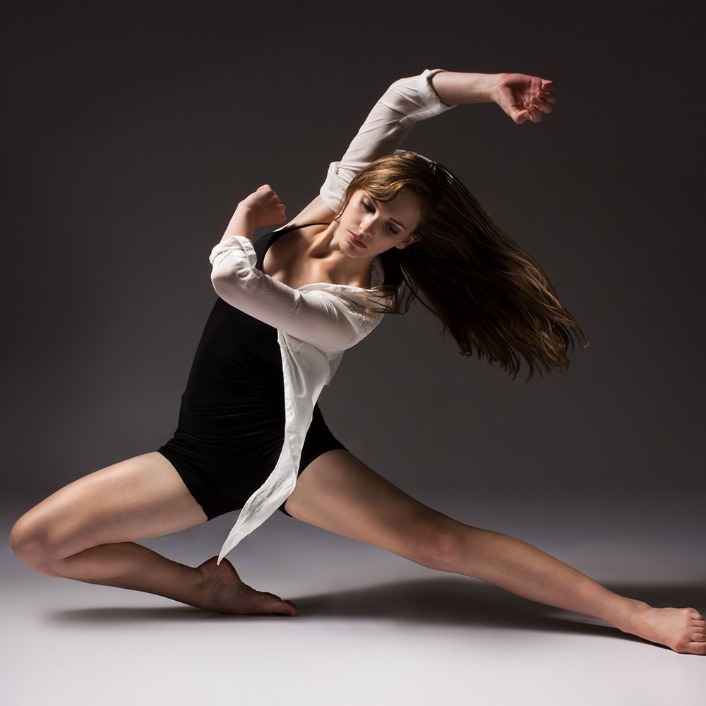Dancer in black shorts, top, and white cardigan, posed dramatically. Grey studio background.