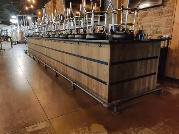 Long bar with metal beer taps in a rustic restaurant interior, viewed from the side, all barstools are upside down on top of the bar