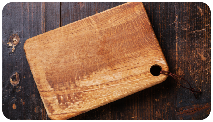 Wooden cutting board on a dark rustic table with a leather hanging strap.