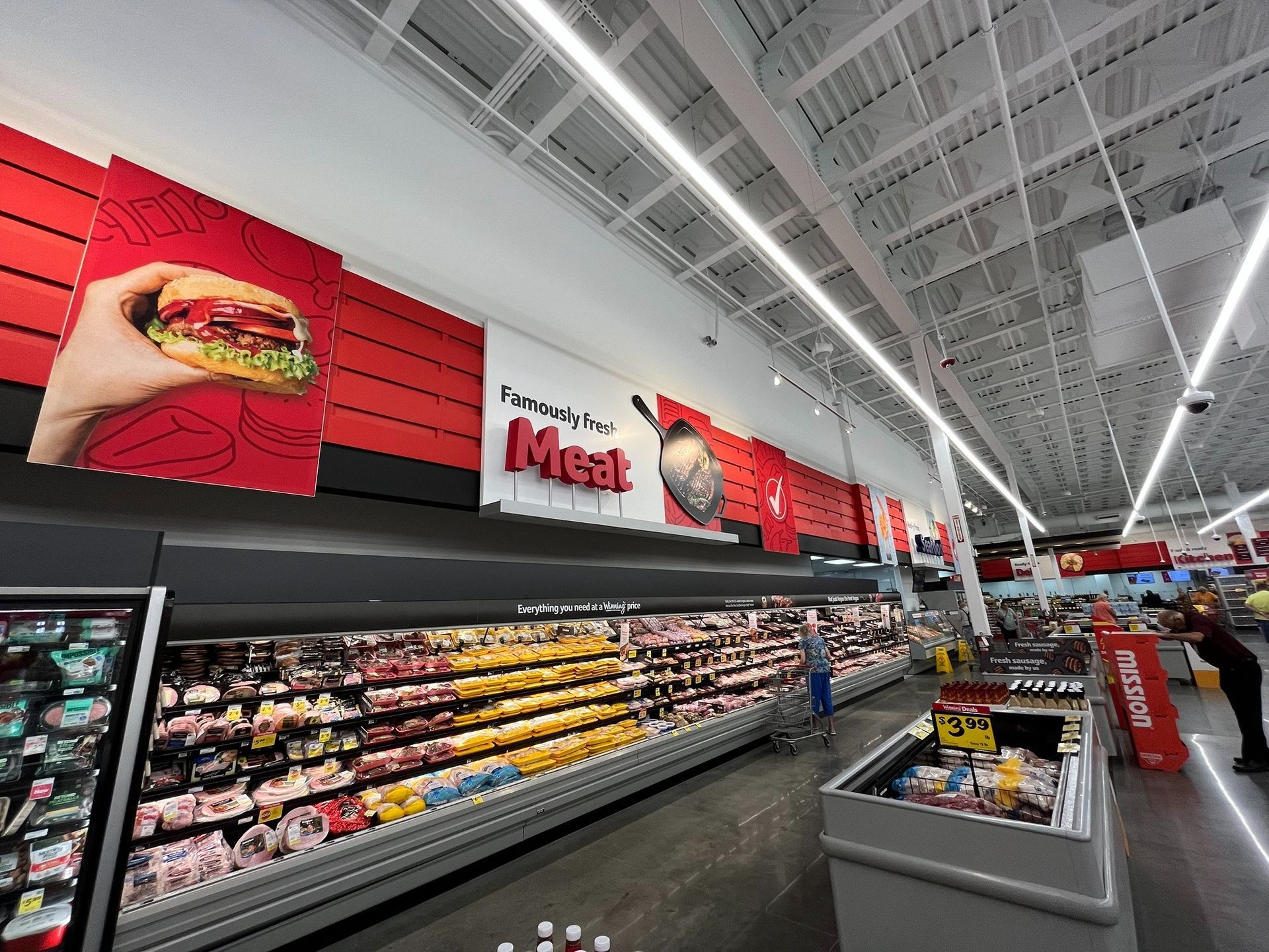 Grocery store meat and deli aisle with red sale signs and refrigerated meat displays