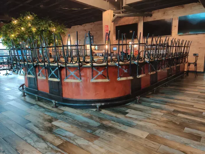 Upside-down chairs stacked on tables in a dimly lit restaurant, with a wooden floor and booth seating.