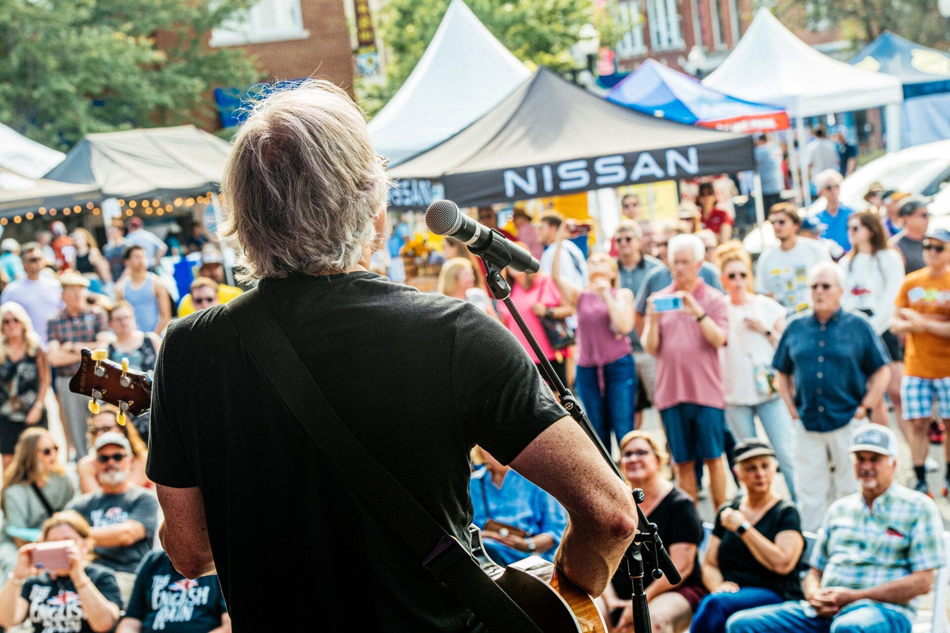 People walking outdoors at an event, many wearing blue shirts, some holding signs on a sunny day.