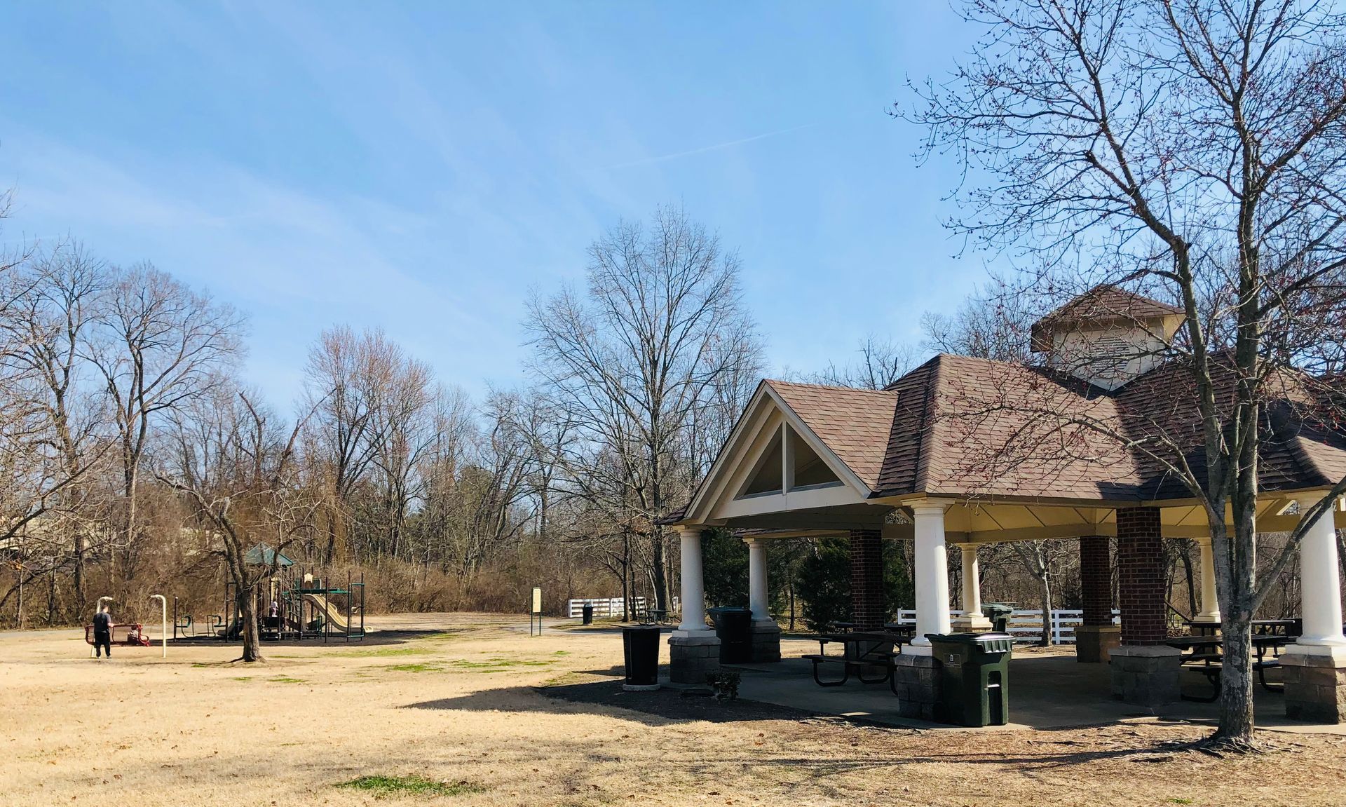 Park scene with gazebo, bare trees, and playground on a sunny day.