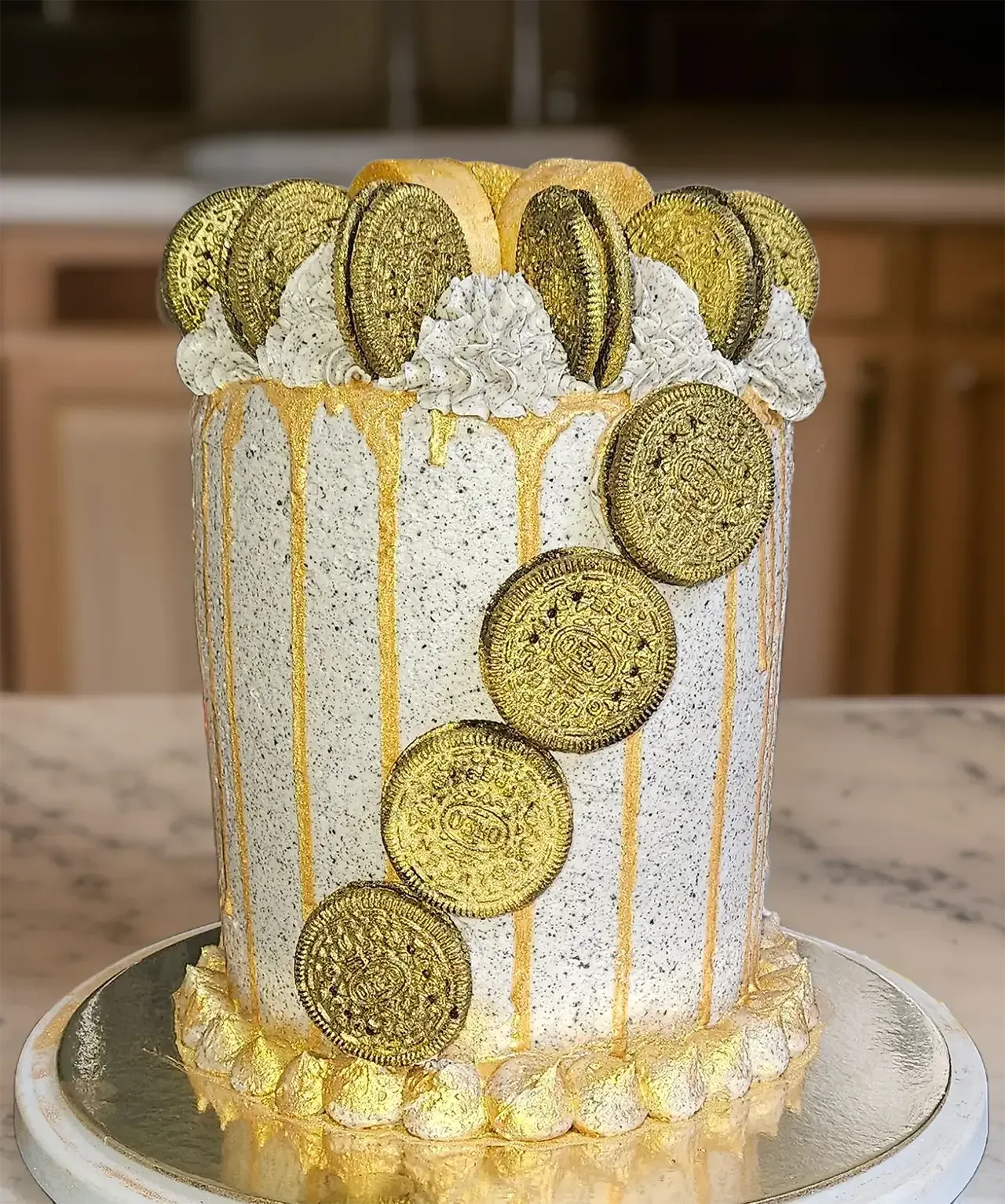 A white cake with gold icing and cookies on top is sitting on a table.