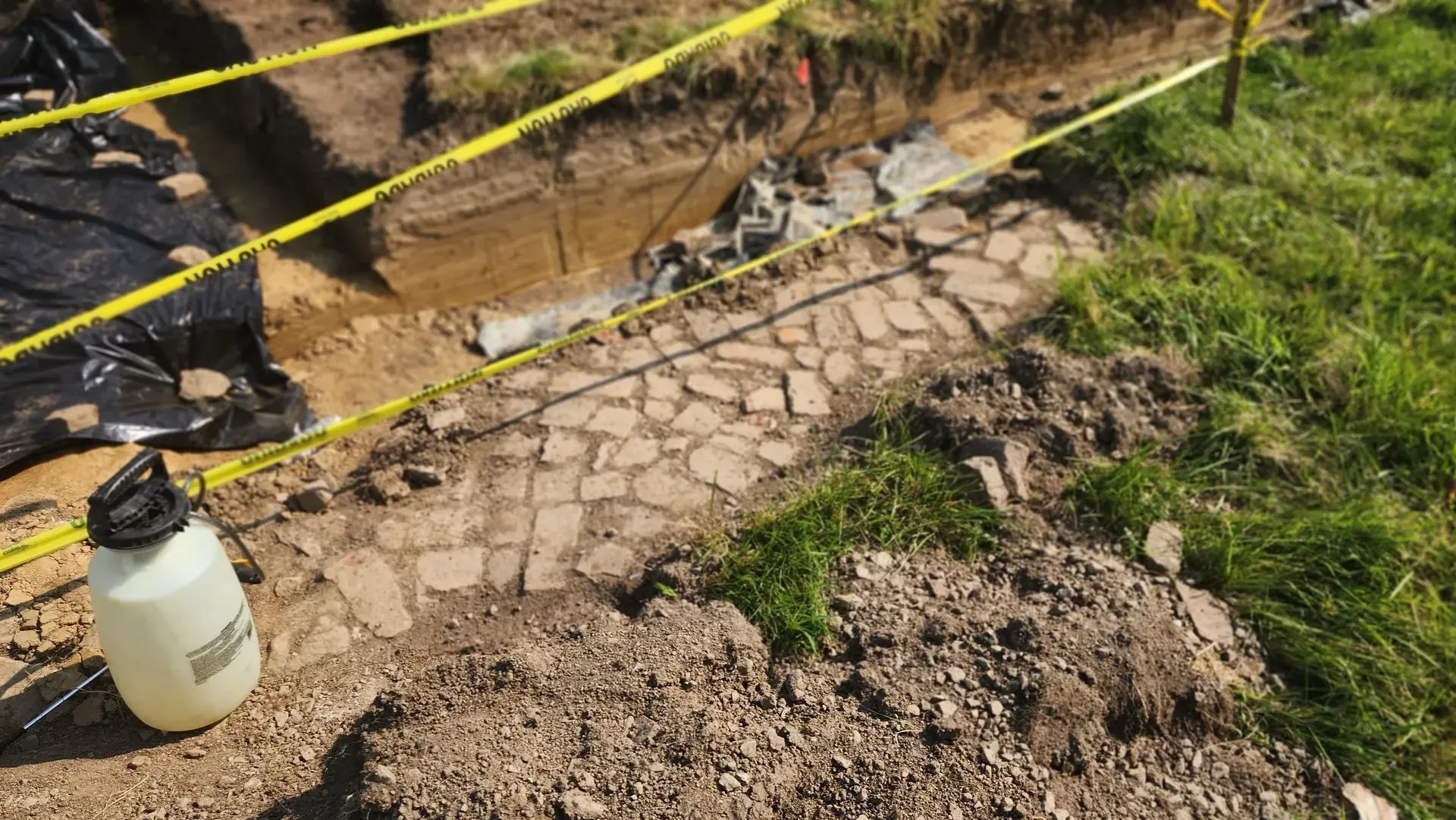Excavation site with a brick road partially uncovered. Yellow tape surrounds the area.