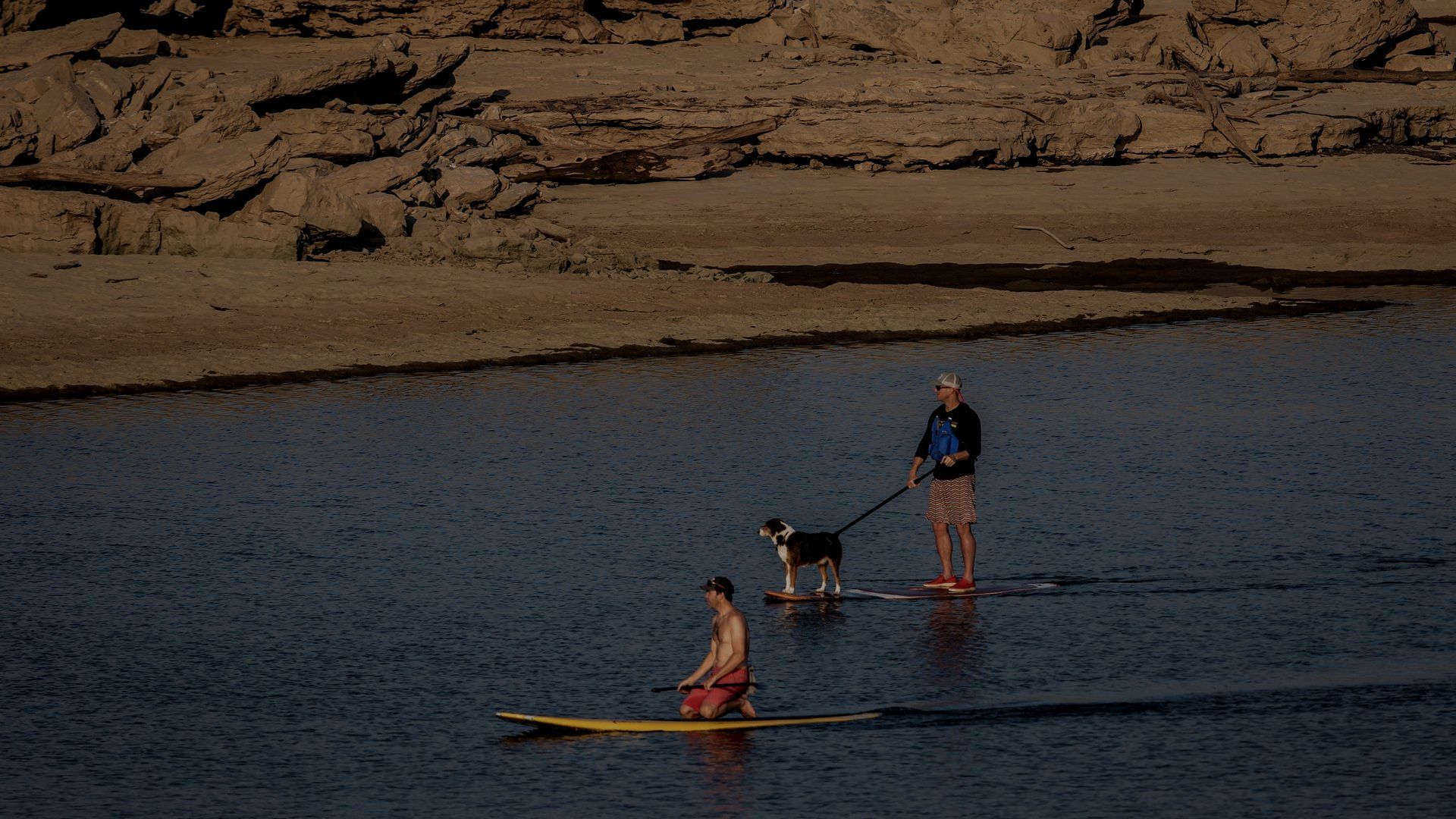 A man and a dog are standing on a paddle board in the water.