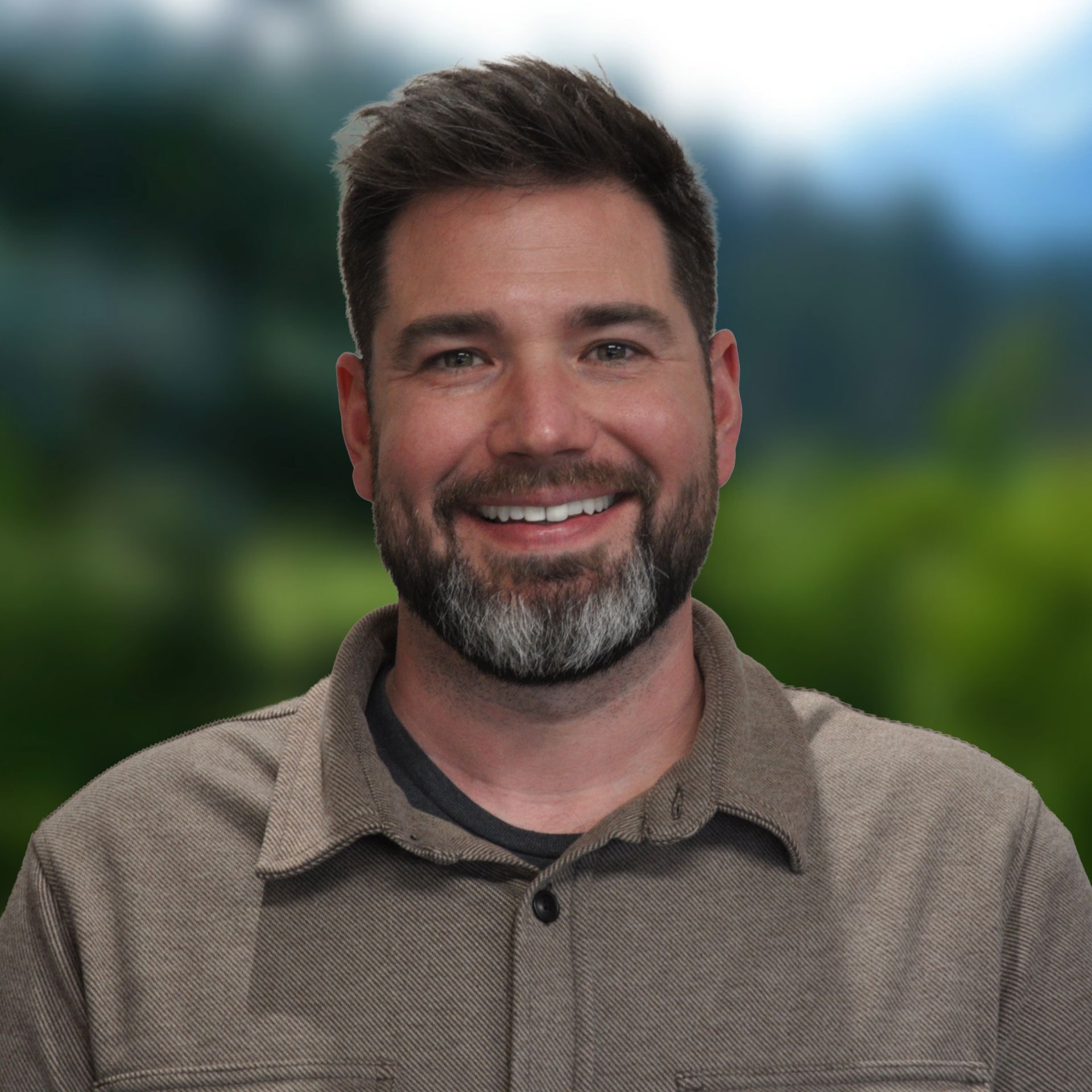 Melissa in blue top smiles at camera, blurred green background.