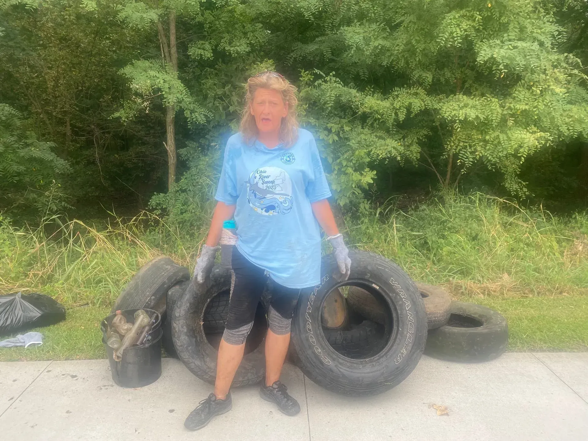 Woman in blue shirt and gloves stands near tires, outdoors.