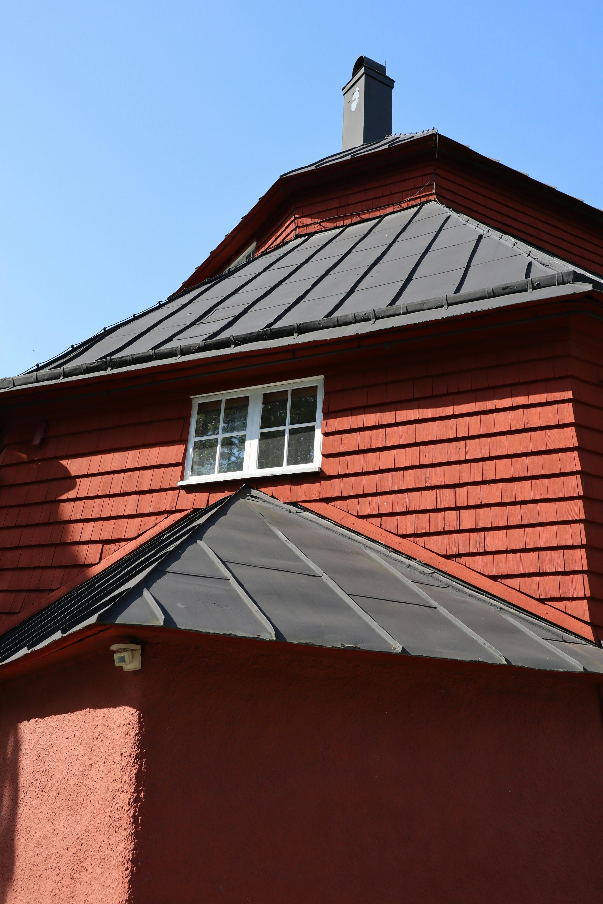 Red wooden building with black metal roof and white-framed window against a blue sky in Central PA