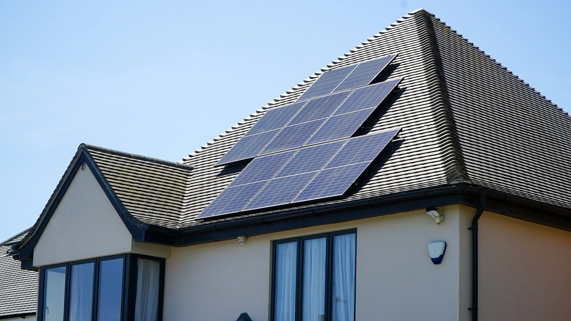 Solar panels on a residential roof, installed in a zigzag pattern, blue and black against a pale roof.