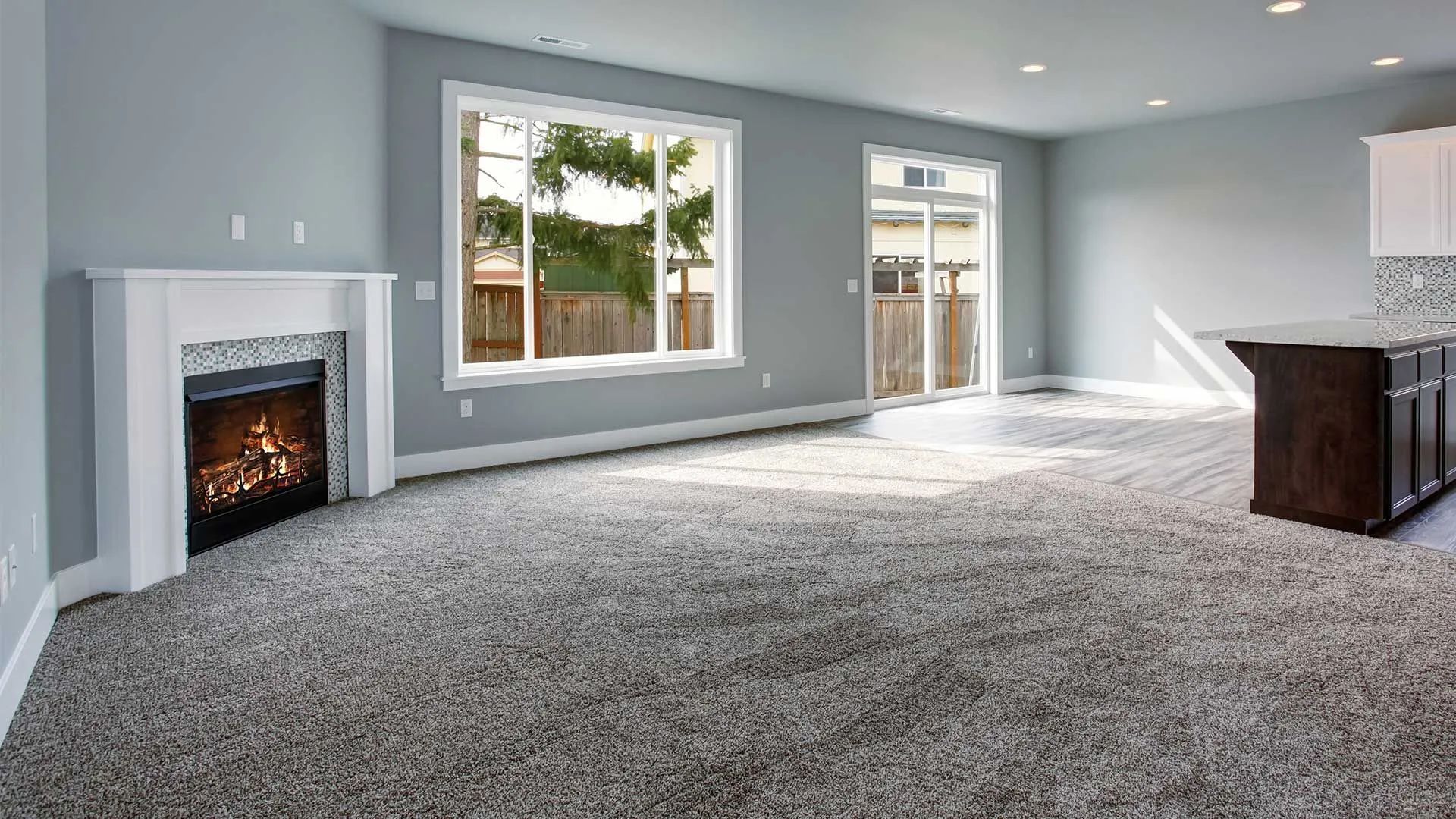 Spacious gray living room with fireplace, carpeted floor, large windows, and sliding glass doors.