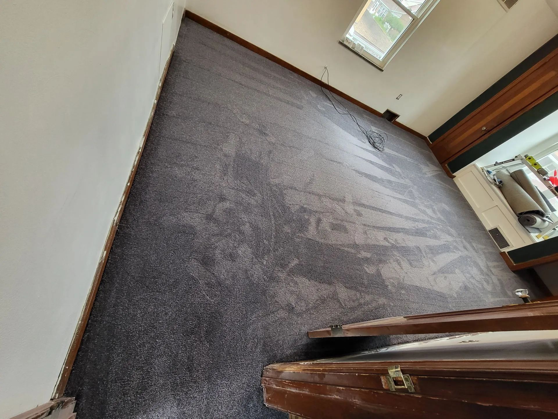 A room with dark gray carpeting, white walls, and a window, viewed from a high angle near a wooden door frame.