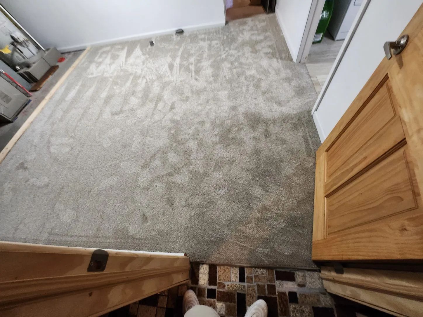 Overhead view of a gray carpeted room with wooden cabinets and a brown tiled entryway.
