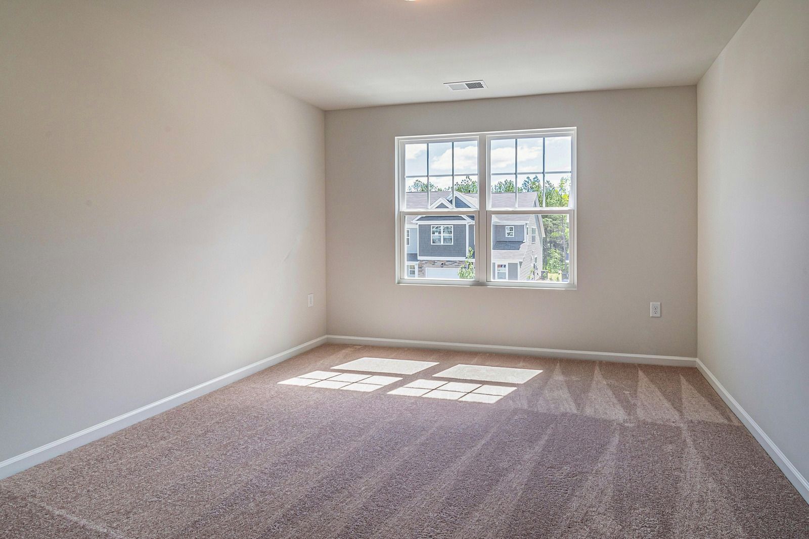 Empty room with carpet, window, and neutral-colored walls. Sunlight shines through the window onto the floor.