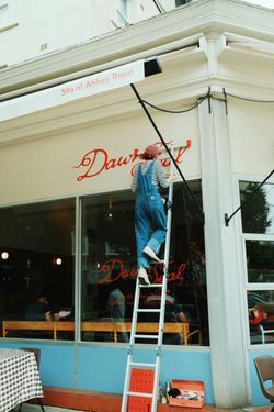 Person on a ladder fixing the awning of a restaurant called 