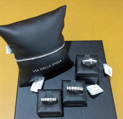 Esposizione di gioielli: due anelli su blocchi, orecchini pendenti, un braccialetto su una scatola blu, su sfondo giallo.