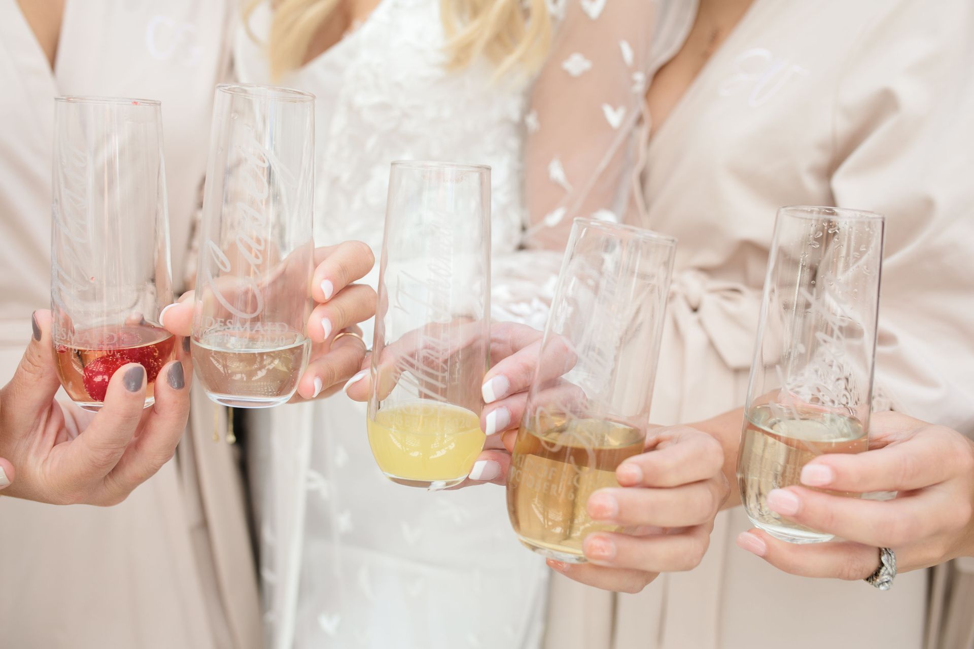 People in robes holding clear, etched stemless champagne flutes filled with various drinks for a celebratory toast.