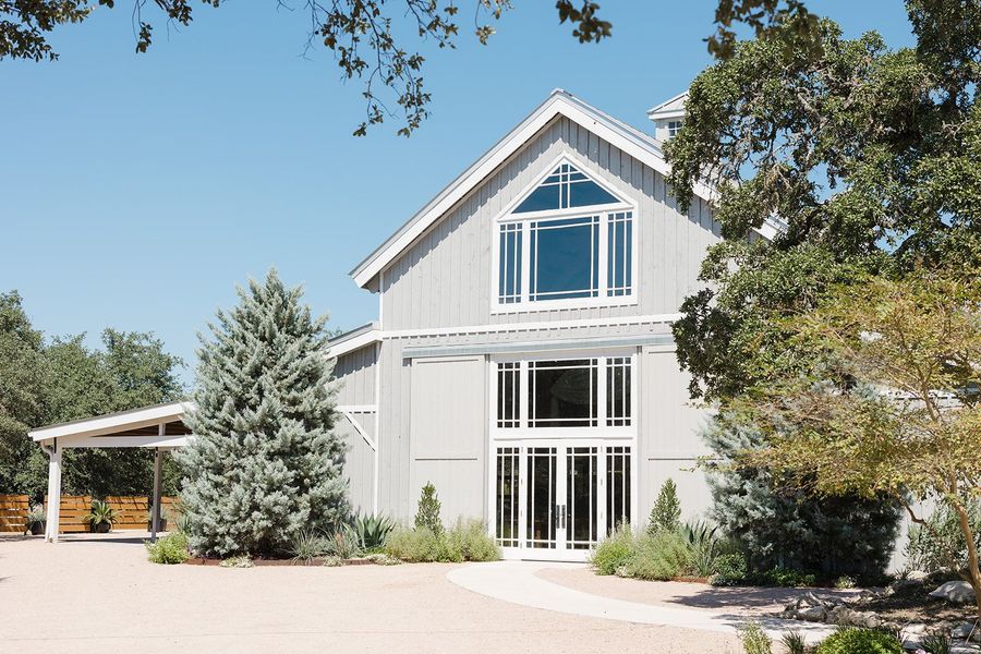 Gray barn at The Addison Grove with large windows, surrounded by trees under a blue sky.