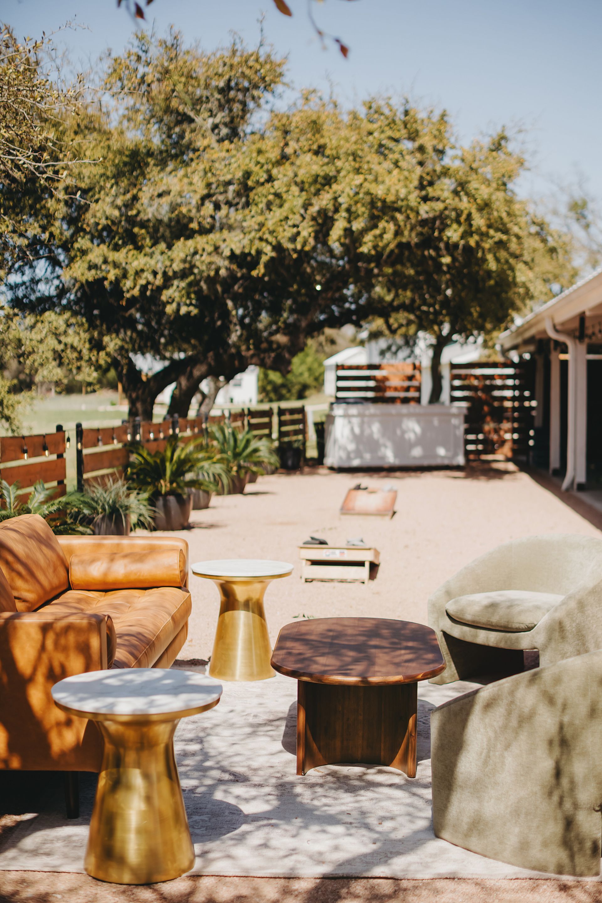 An outdoor seating area on a patio featuring a leather sofa, two armchairs, a wooden coffee table, and gold side tables.