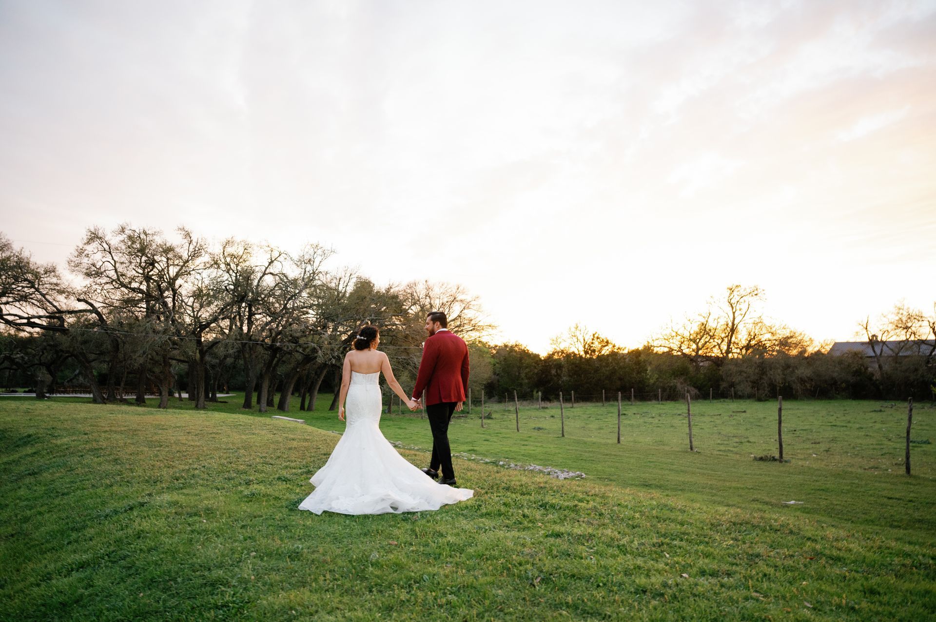 A high-angle view of a rustic barn reception hall with round tables, white linens, and peach-colored draped ceiling fabric.