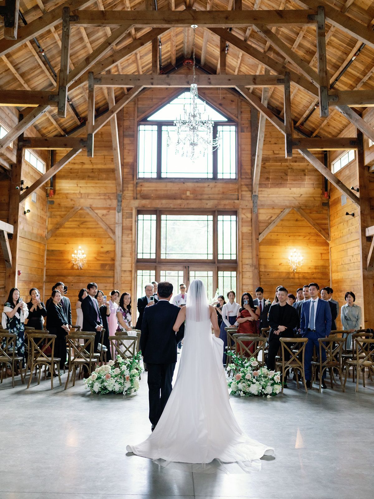 A couple walking down the aisle in a rustic wooden barn venue with guests seated on both sides.