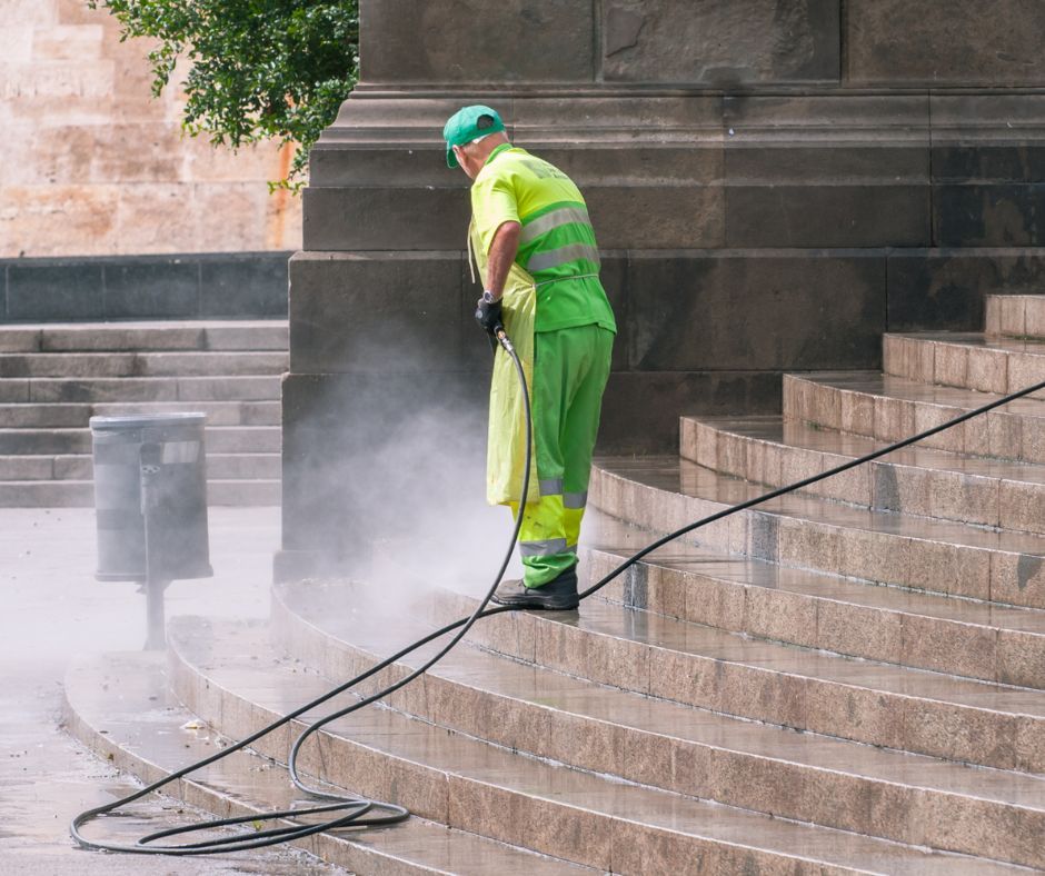 A man is cleaning the steps of a building with a high pressure washer.