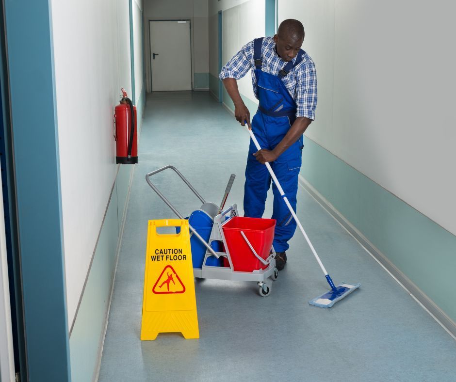 A man is mopping a hallway next to a caution wet floor sign