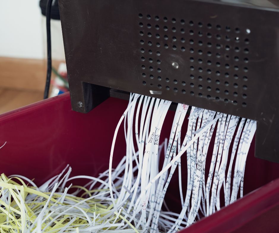 Shredded paper is coming out of a machine in a red bin