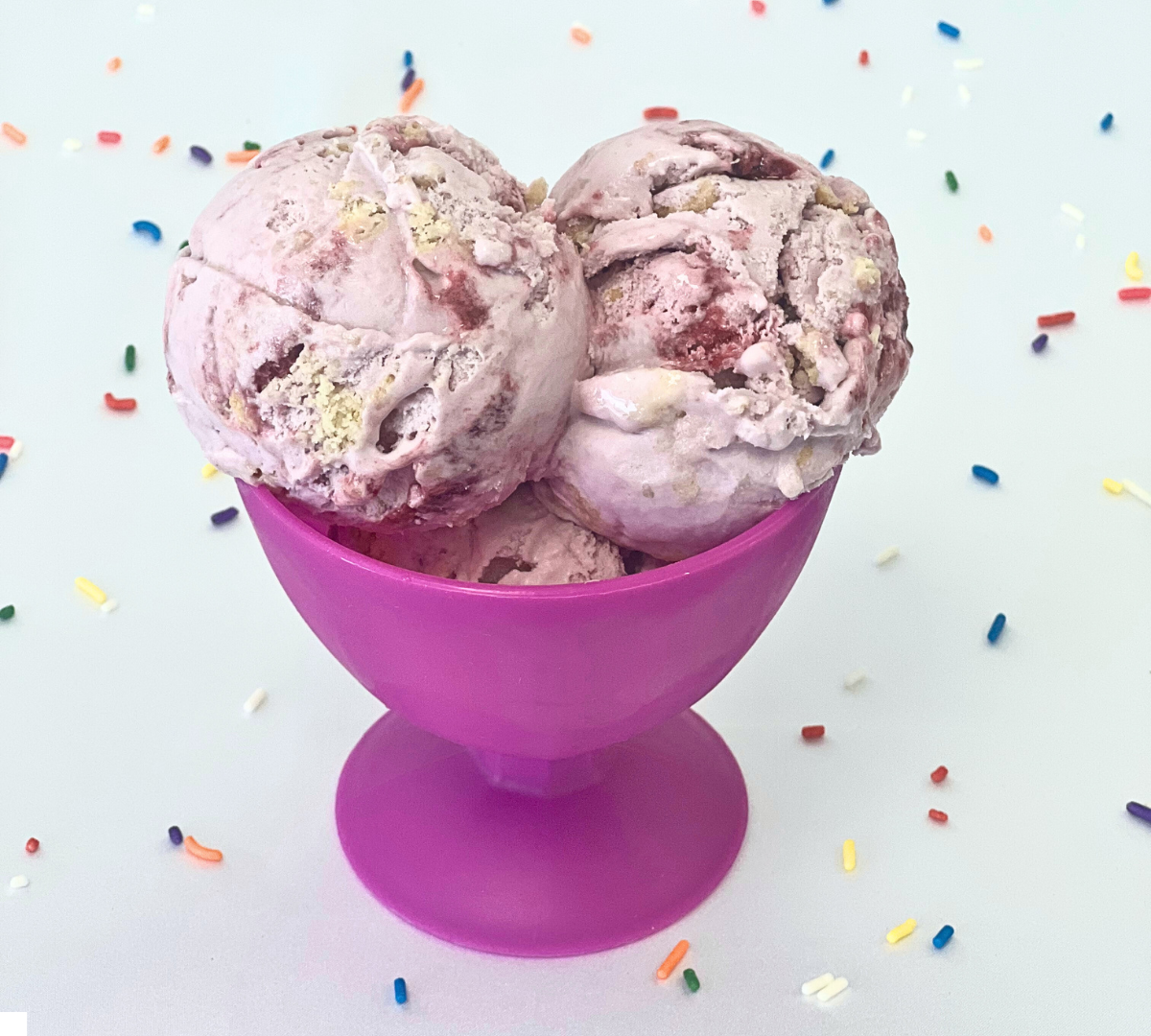 Three scoops of ice cream are in a purple bowl surrounded by sprinkles.