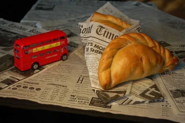 A red double decker bus sits next to a pastry on a newspaper
