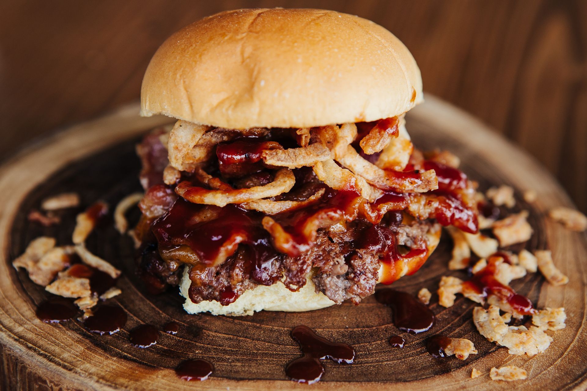 A hamburger with onion rings and barbecue sauce on a wooden cutting board.