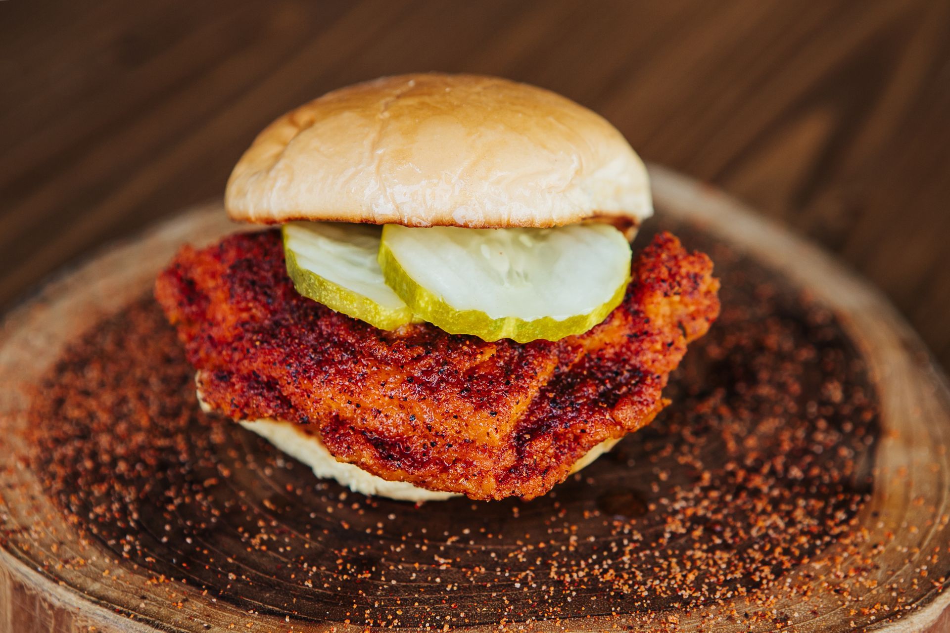 A chicken sandwich with pickles on a bun on a wooden cutting board.