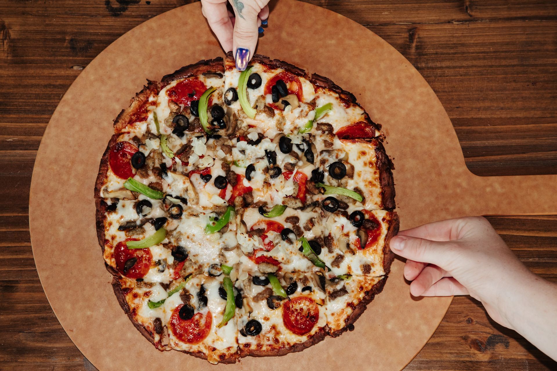 A person is taking a slice of pizza from a wooden cutting board at 14 Mill Market in Nixa Missouri