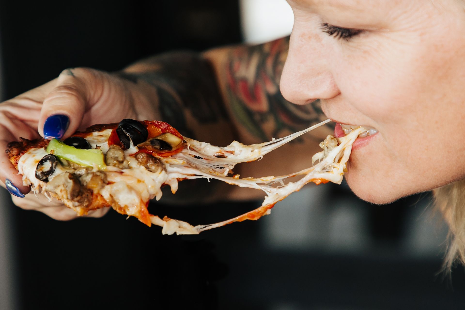 A woman is eating a slice of pizza with cheese coming out of her mouth.
