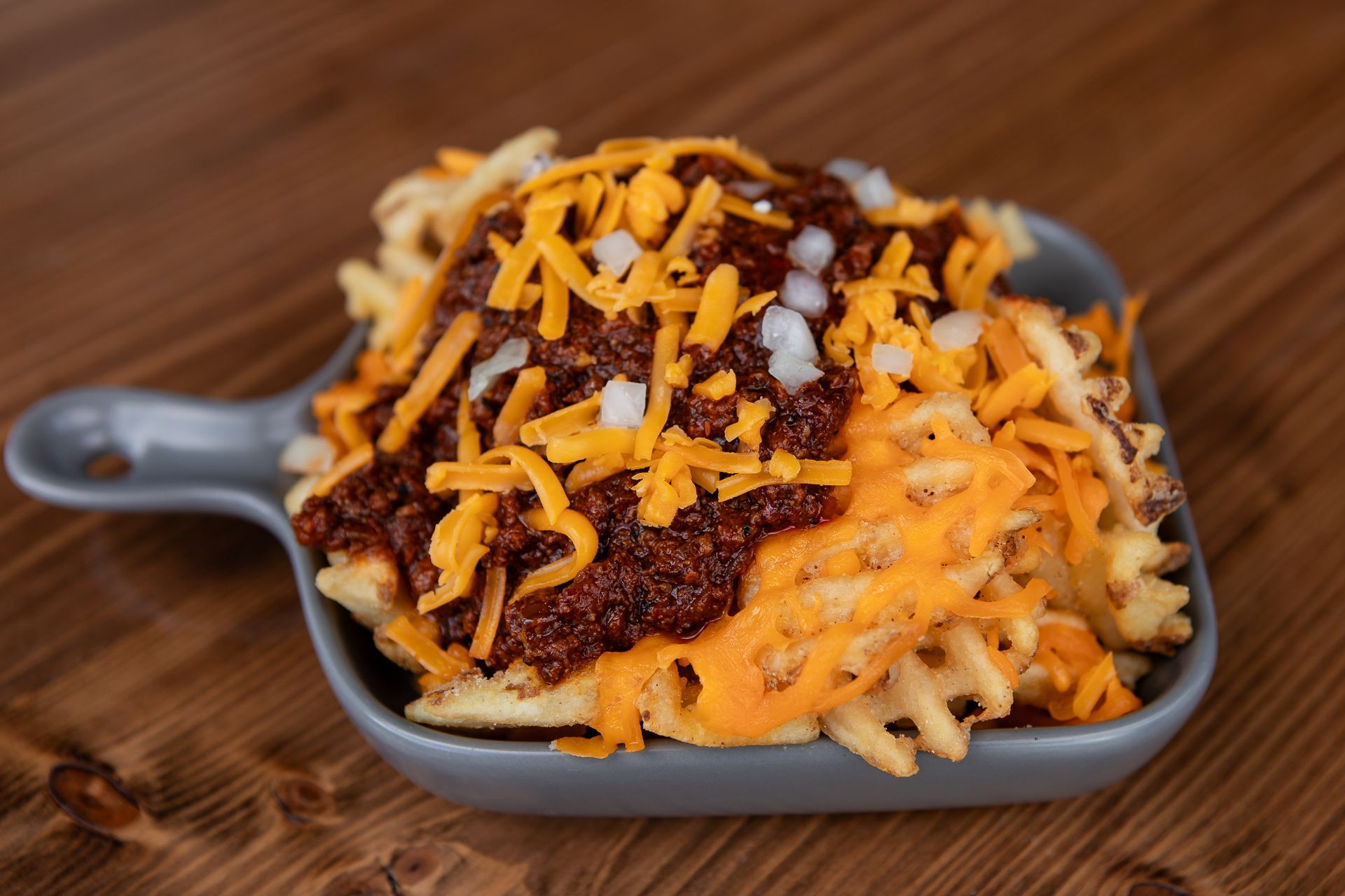 A bowl of french fries with chili and cheese on a wooden table.