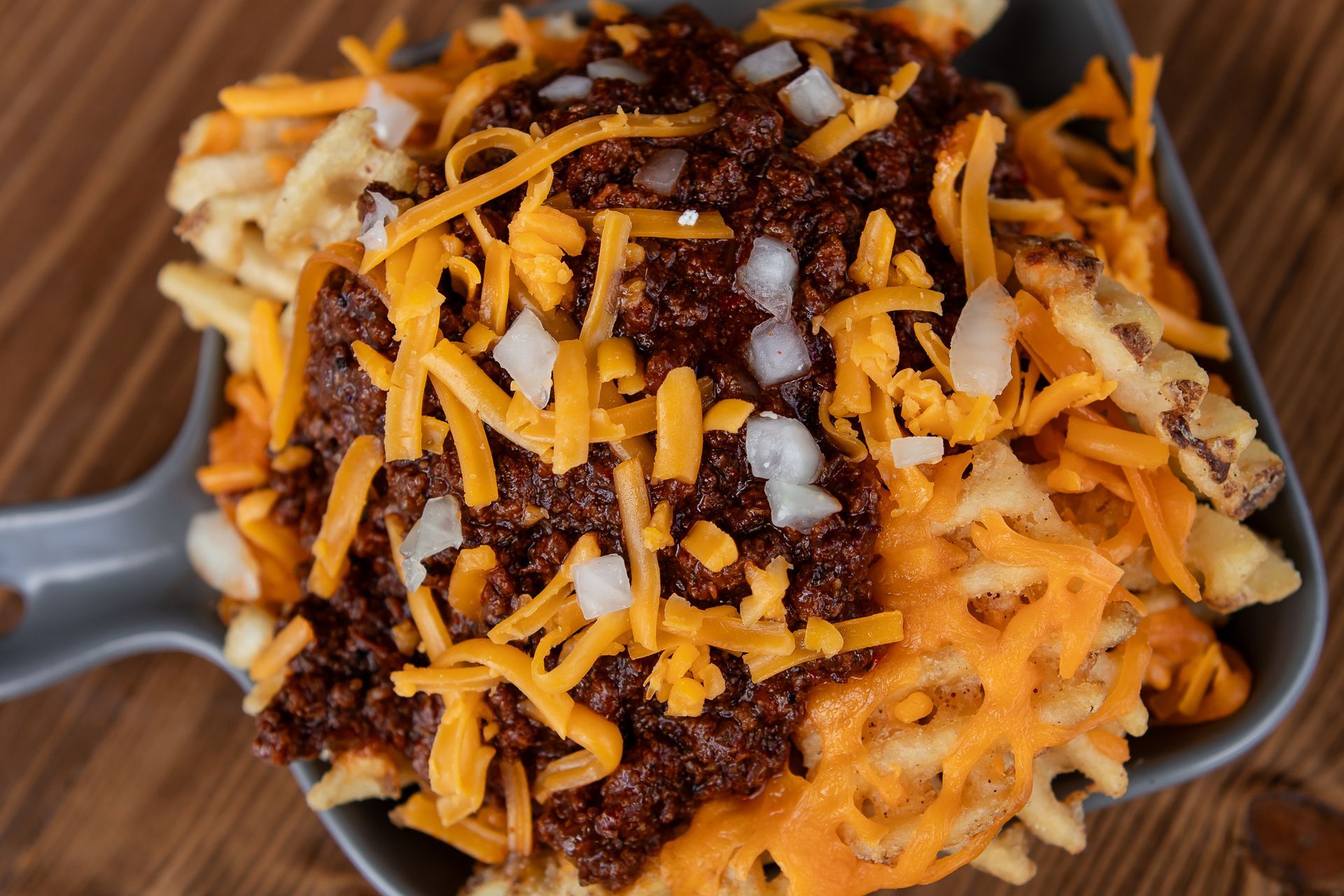 A close up of a skillet filled with french fries , cheese , and chili.