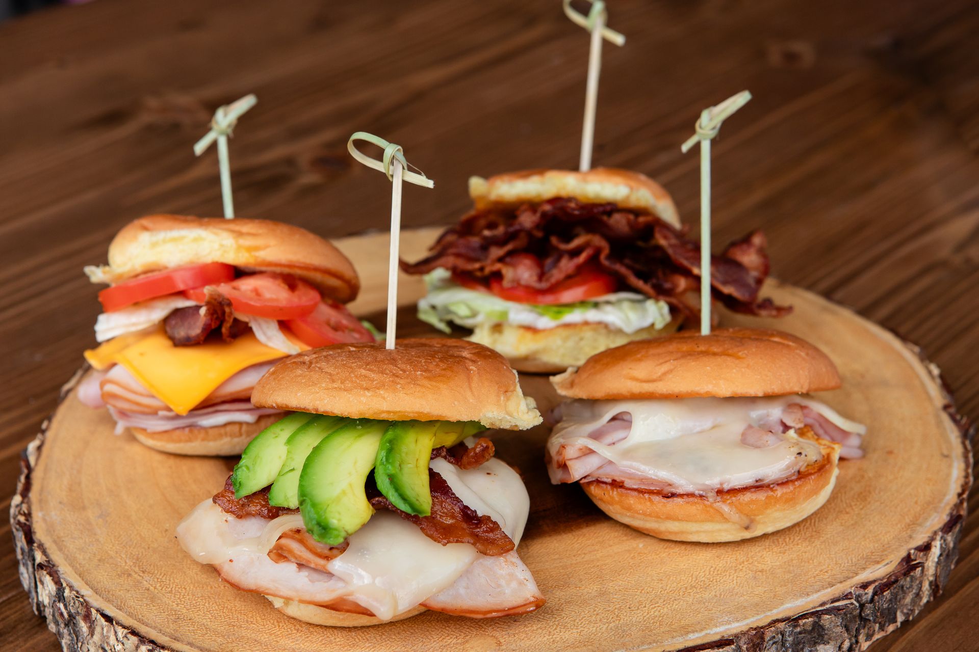 Three sandwiches are sitting on a wooden cutting board on a wooden table.