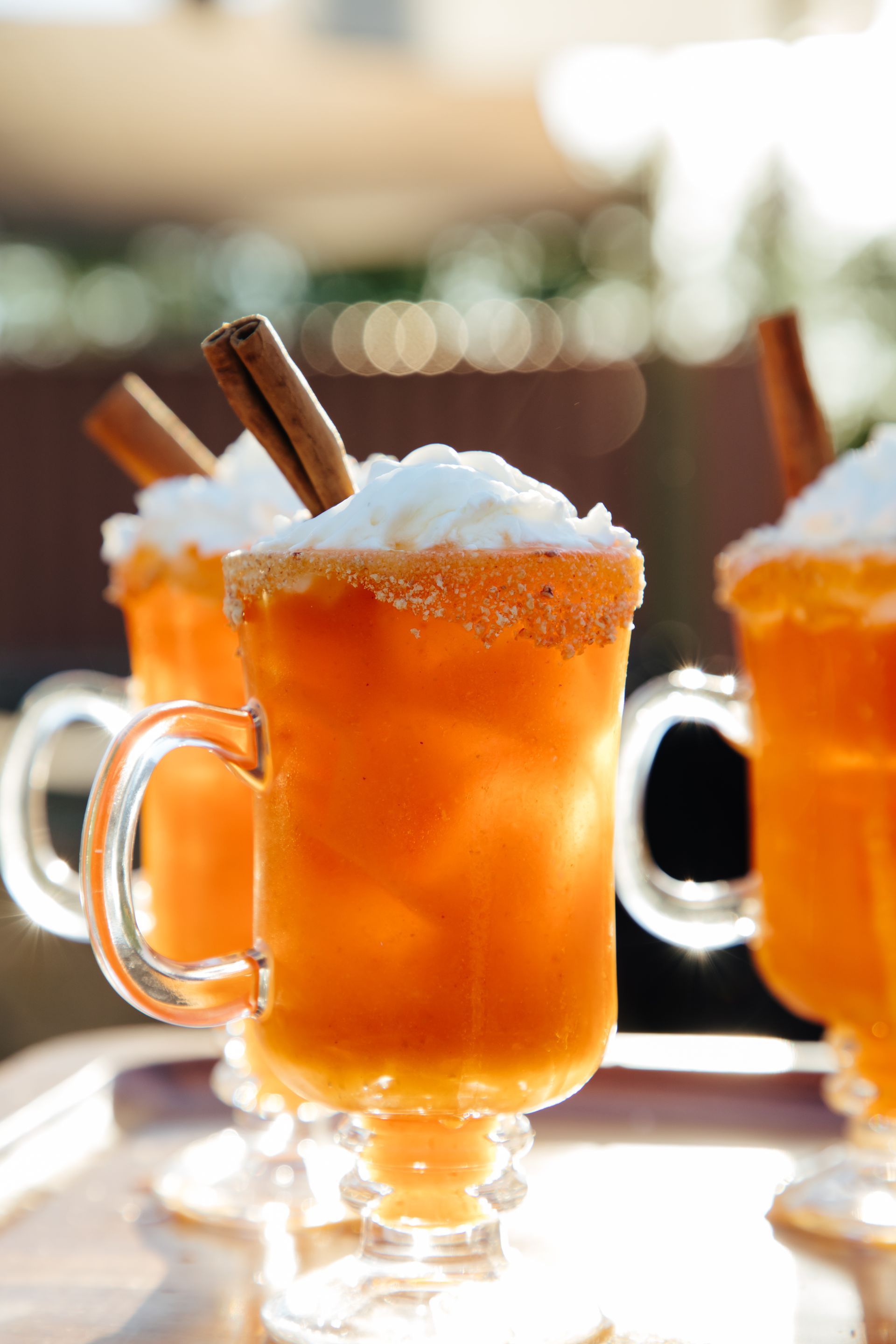 Three cups of orange liquid with cinnamon sticks and whipped cream on top.