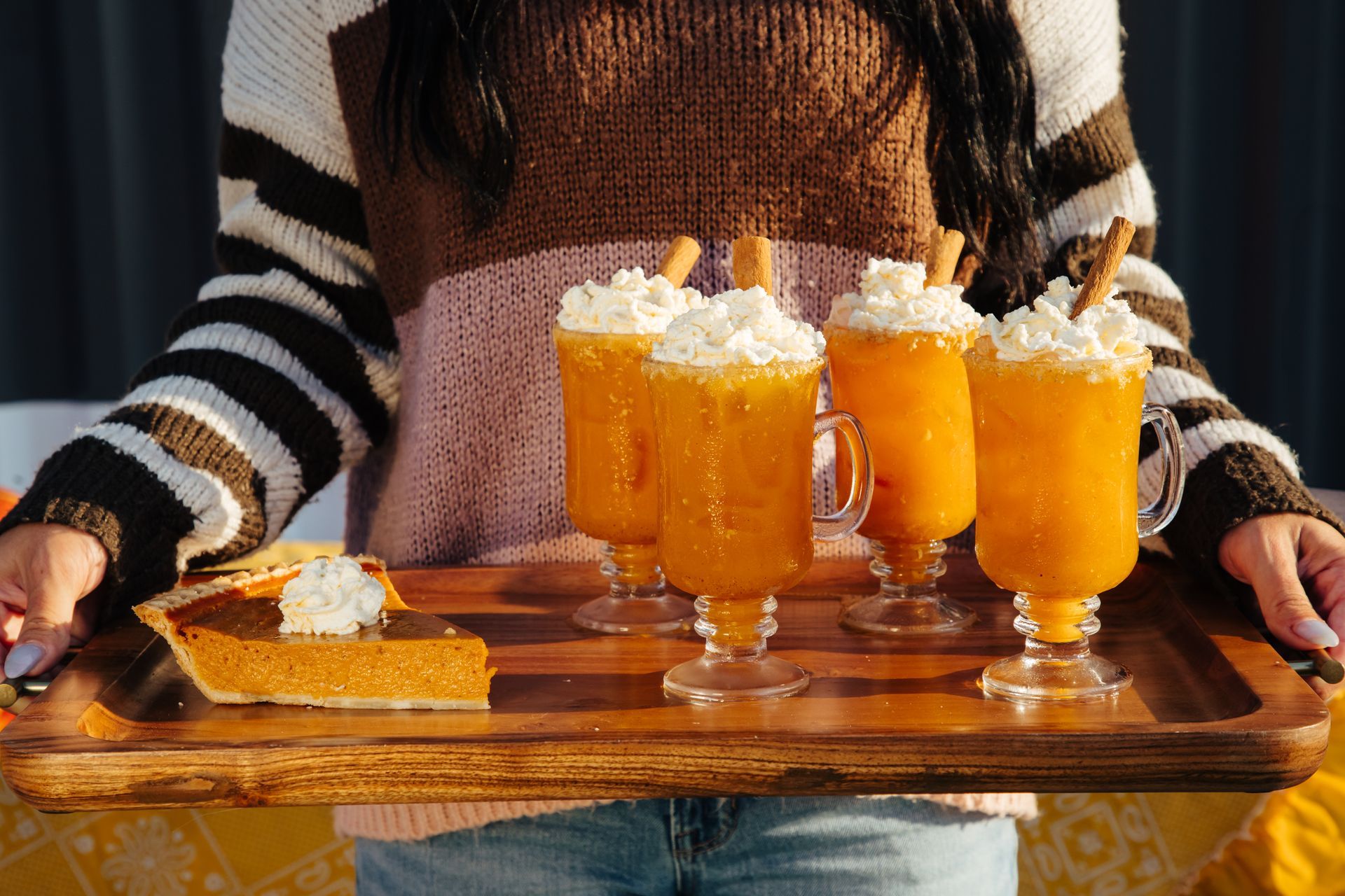 A woman is holding a tray of drinks and a piece of pumpkin pie.
