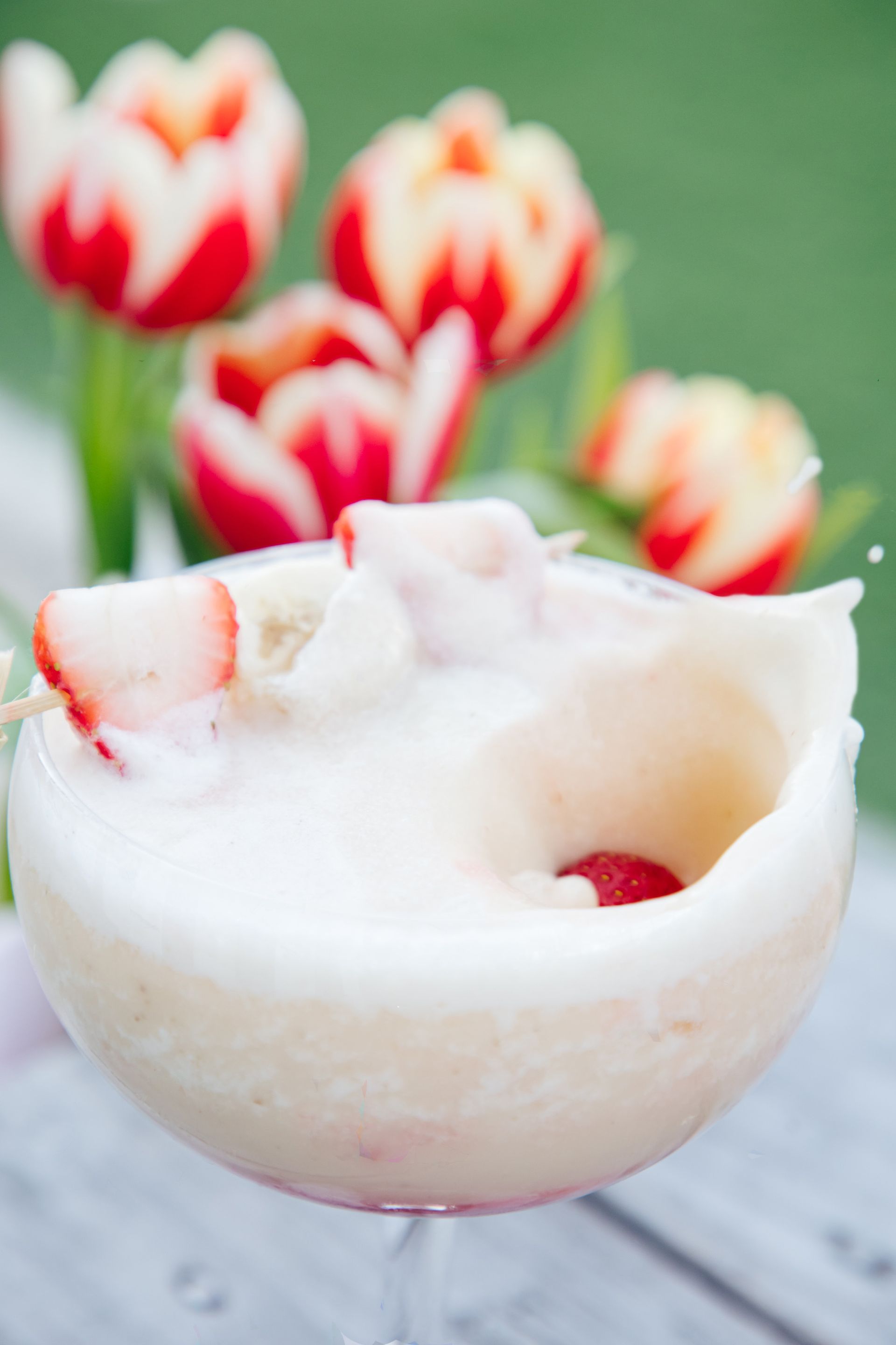 A martini with strawberries in it and flowers in the background